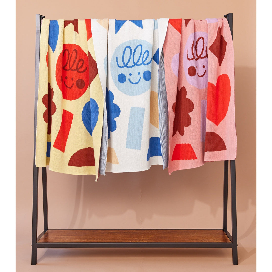 A trio of playful knit blankets draped over a clothes rack.