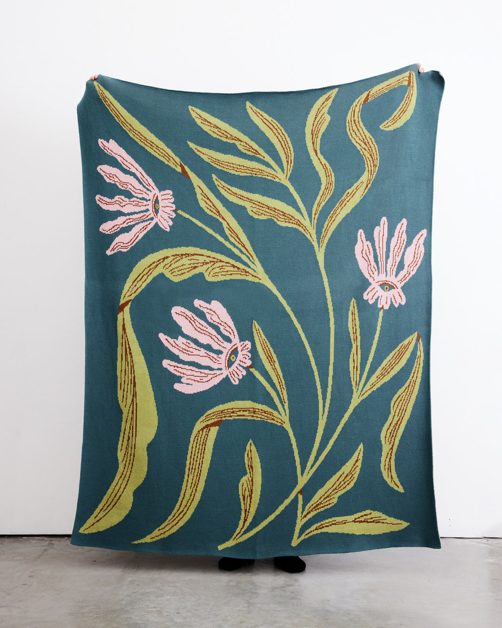 Floral-patterned blanket with pink flowers and green leaves on a teal background