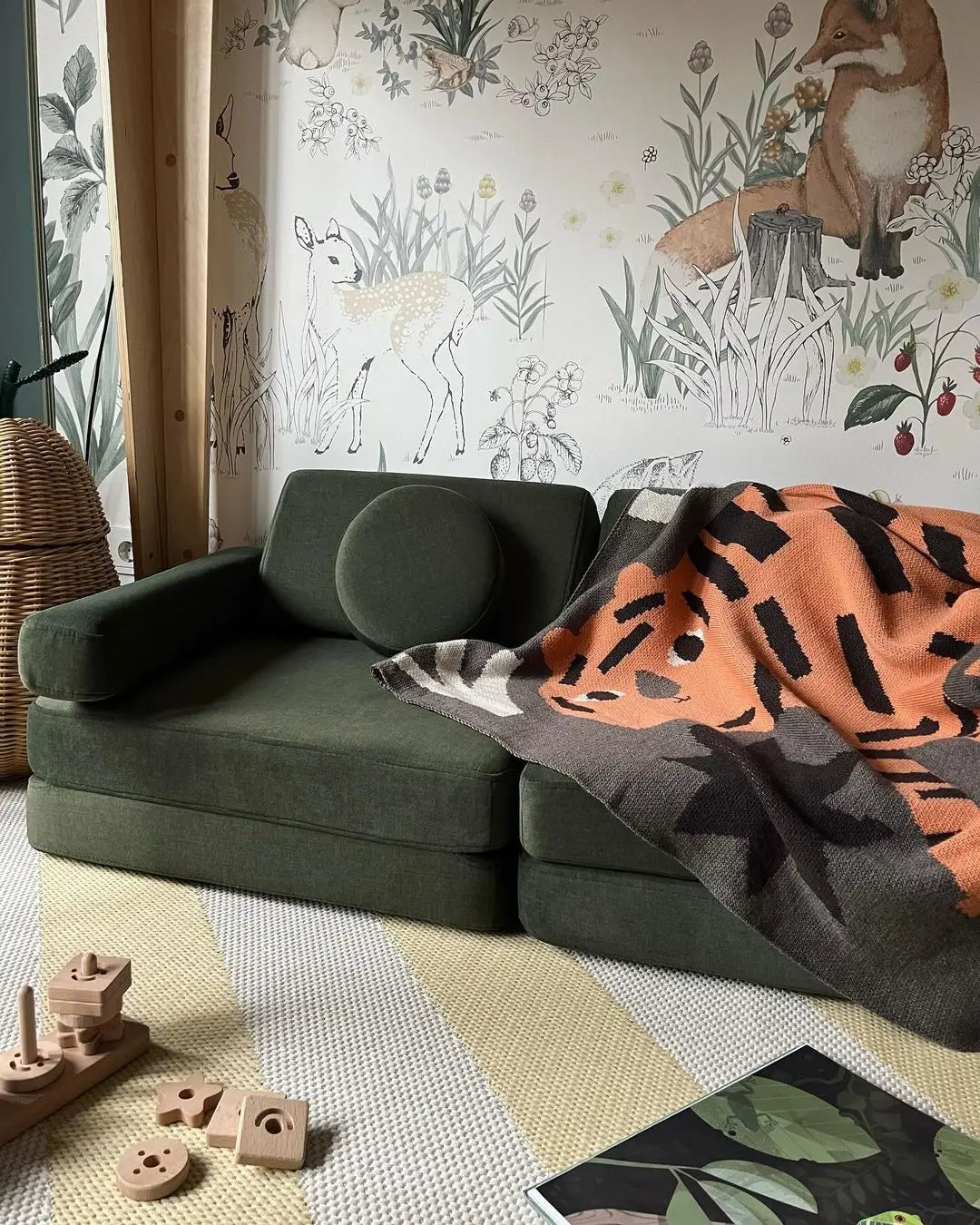 Green sofa with a tiger-patterned blanket against a wall with animal-themed wallpaper.