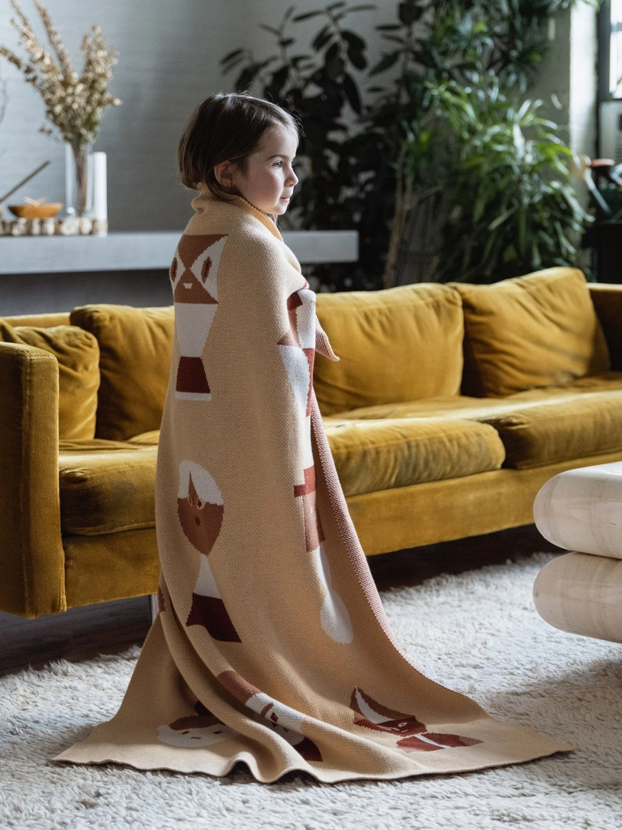 Young child wrapped in a cozy Biquette Mix & Mingle Midi knit blanket designed by Beth Haidle, showing its soft texture and child-friendly size